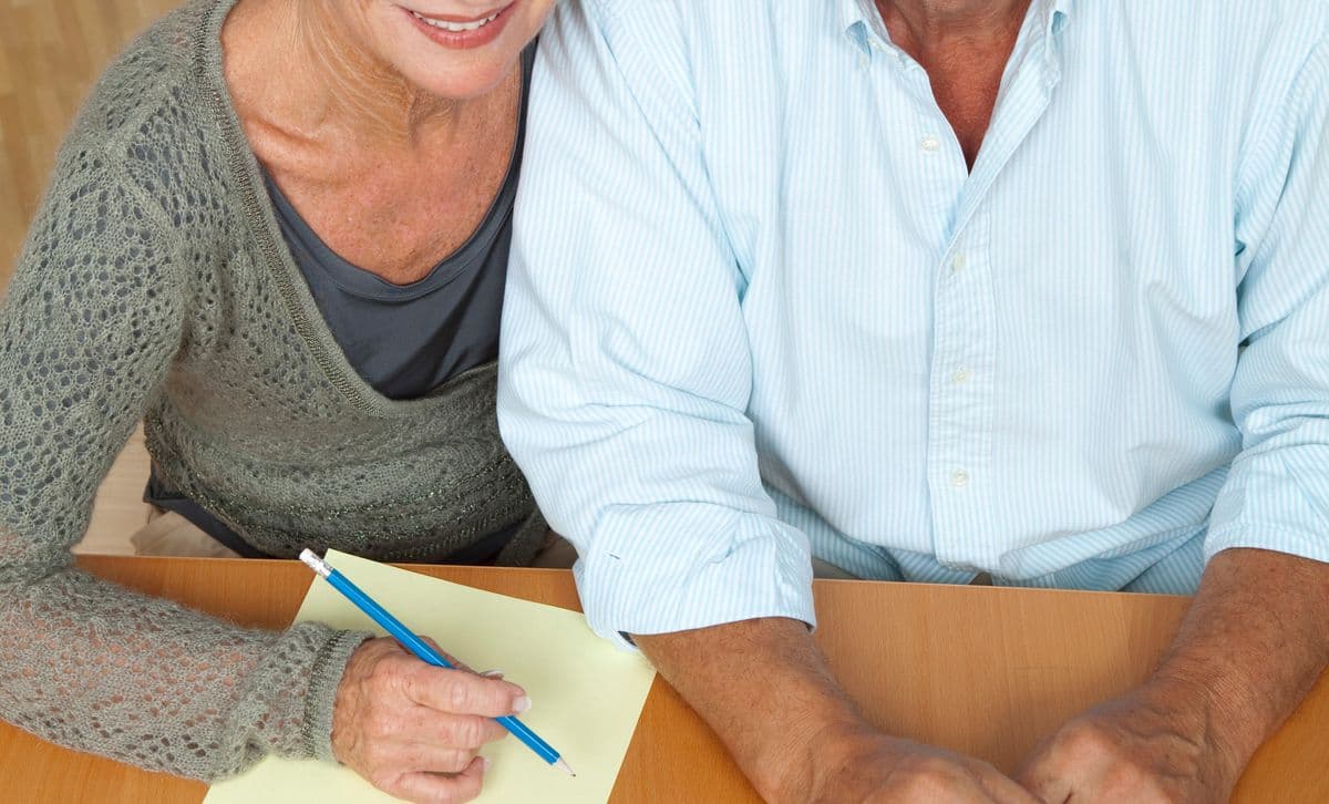 An older couple working through paperwork together at a kitchen table